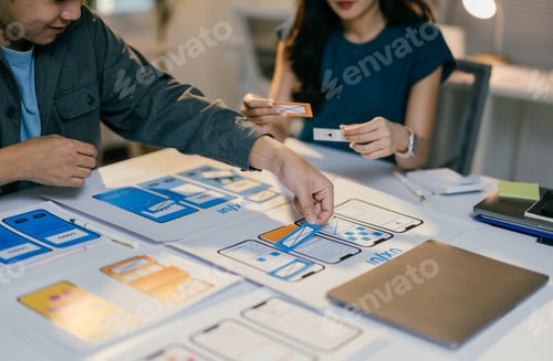 Preview: Two web designers are placing cutouts of buttons and icons onto a paper prototype of a mobile applic