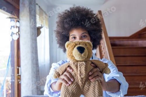 Preview: Portrait of young african american female nurse in medical uniform holding stuffed toy showing care
