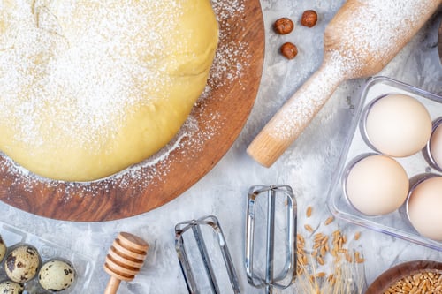 Preview: Overhead view of raw pastry flour on round board grater eggs on stained white background