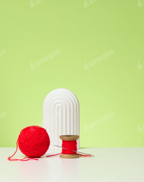 Preview: Red ball with woolen thread and large needle on white table, green background