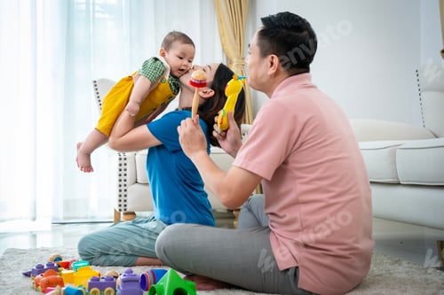 Preview: A man and a woman are holding a baby. The baby is wearing yellow shorts. The man is holding a toy in