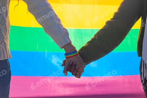 Preview: Interracial couple holding hands with rainbow bracelet and lgbtq plus flag