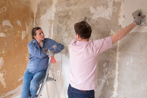 Preview: Young couple removing old wallpaper from walls preparing for flat renovation.