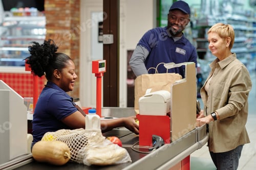 Preview: Happy young female cashier scanning food products chosen by customer