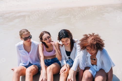Preview: Four young women are sitting on the beach, enjoying the sun