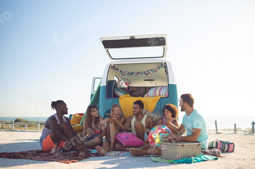 Preview: Front view of group of diverse friends interacting with each other near camper van at beach