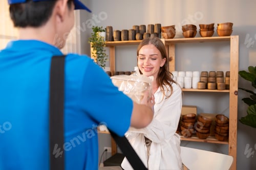 Preview: An Asian delivery man wearing blue uniform sending food to young woman customer in her shop