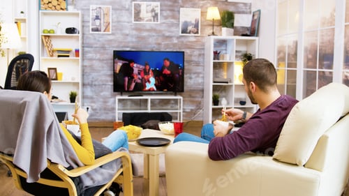 Preview: Young couple smiling while watching tv sitting on sofa