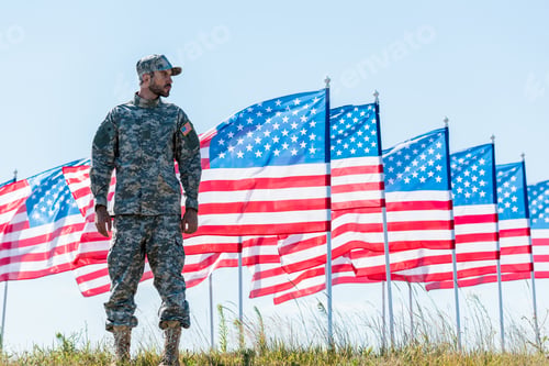 Preview: patriotic soldier in uniform standing near american flags and blue sky