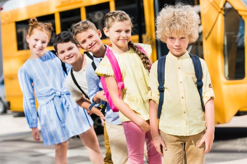 Preview: group of adorable pupils looking at camera while standing in row in front of school bus