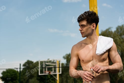 Preview: sexy shirtless sportsman with towel opening bottle of water at basketball court