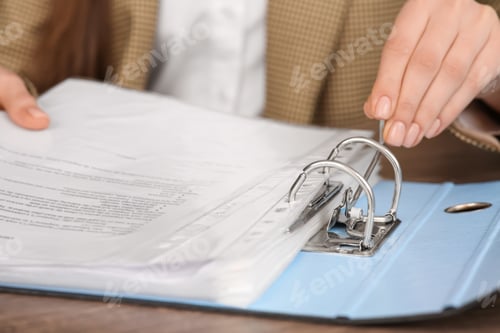 Preview: Businesswoman putting document into file folder at wooden table in office, closeup