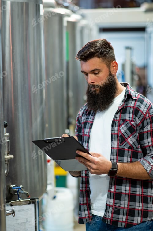 Preview: Man working in brewery and taking notes of the beer production