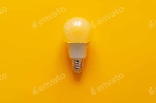 Preview: Light bulb on yellow paper background top view