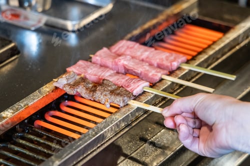 Preview: Hand barbecuing the delicious hida beef with high marbling on skewers at street market.