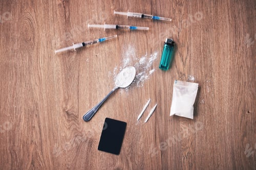 Preview: A spoon with heroin, syringes with with, a blue lighter, a bag and a bank card on a wooden table. A