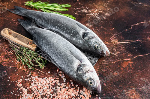 Preview: Seabass or sea bass fresh raw fish on a cleaver with salt and herbs. dark background. Top view