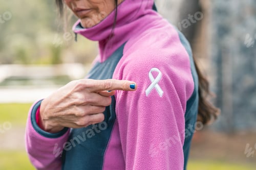 Preview: Woman pointing to an embroidered cancer awareness ribbon with her finger on her sweatshirt