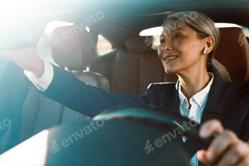 Preview: Mature asian woman looking in rear-view mirror while driving car