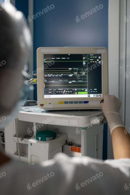 Preview: Gloved hand of young female assistant of surgeon standing in front of display