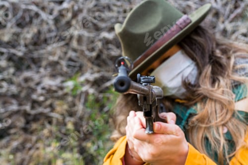 Preview: Blonde scout girl with mask, green vest and green hat aiming rifle at camera.
