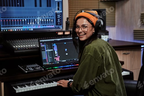Preview: Portrait of beautiful young brunette, female artist smiling at camera while playing keyboard