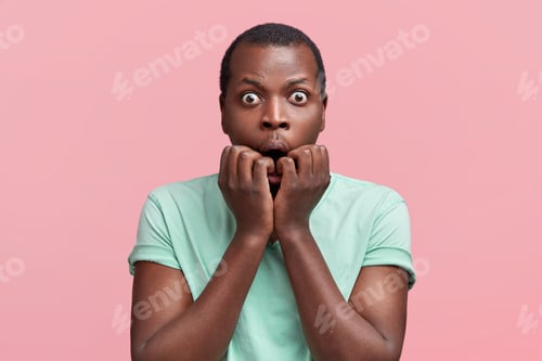 Preview: Surprised nervous dark skinned male student bites finger nails, stares at camera with bugged eyes, b