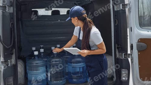 Preview: Delivery woman holding digital tablet near bottle with water in auto on urban street