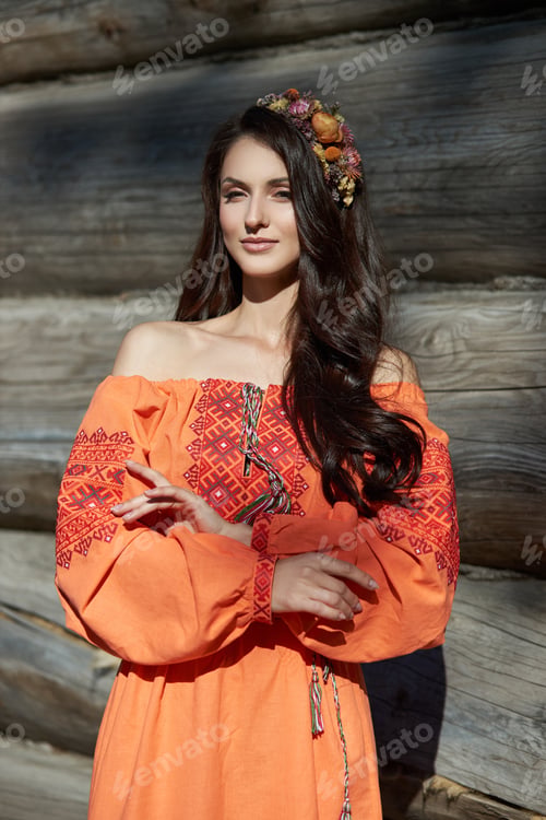 Preview: Beautiful Slavic woman in an orange ethnic dress and a wreath of flowers on her head. Beautiful