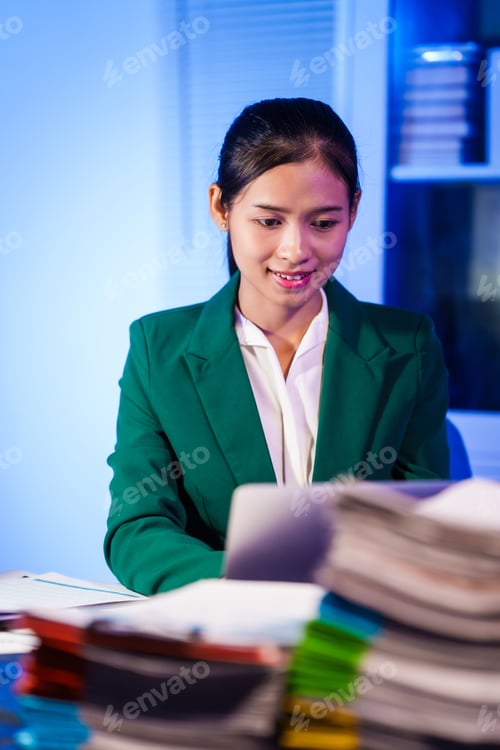 Preview: An Asian businesswoman works overtime,sitting her desk night,searching through numerous documents
