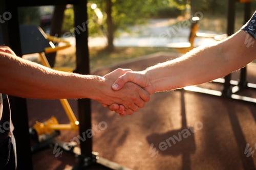 Preview: Male handshake in the street against the background of the sports ground.