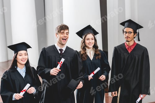 Preview: smiling group on students in graduation gowns holding diplomas
