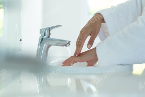 Preview: Mixed race woman wearing bathrobe and washing hands in bathroom
