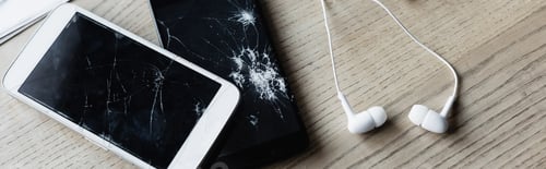 Preview: Top view of earphones with smashed smartphone on wooden background, banner