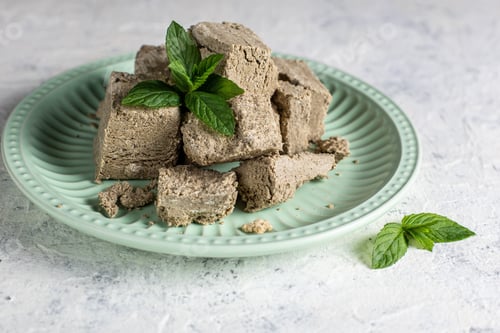Preview: Pieces of halva on green plate. Sweet dessert with mint leaves on white background