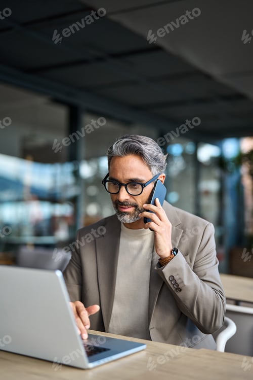 Preview: Busy mature business man talking on cellphone working on laptop outside office.
