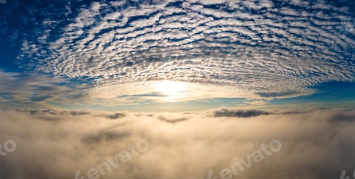 Preview: Aerial view of bright yellow sunset over white dense clouds with blue sky overhead.