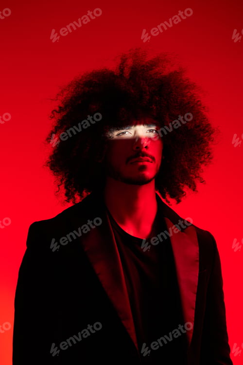 Preview: Fashion portrait of a man with curly hair on a red background, multinational, colored light, trendy