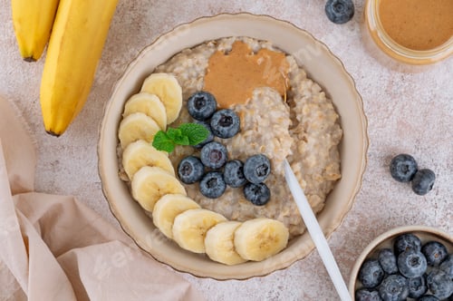 Preview: Oatmeal with milk, berries, sliced banana and nut butter in a bowl. Healthy breakfast. Top view.