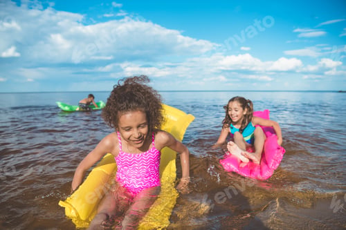 Preview: multicultural happy girls swimming on inflatable mattresses at sea together