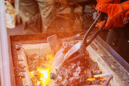 Preview: Craftsman working with glowing coals forge tools in traditional blacksmith workshop