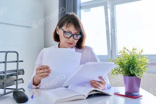 Preview: Middle-aged female working at home at a table with papers