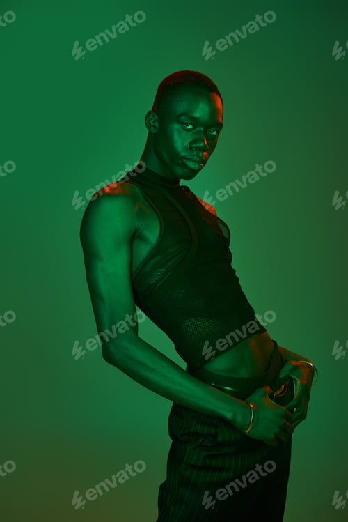Preview: Young man showcases vibrant style and confidence in striking green light during a fashion shoot