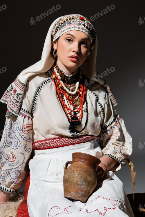 Vista previa: pretty ukrainian woman in traditional clothing with ornament holding clay pot on black