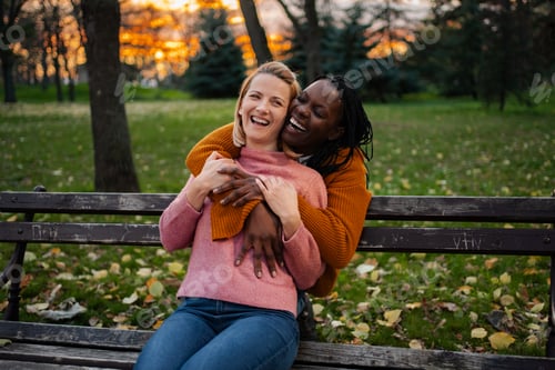 Preview: Happy diverse lesbian couple embracing in autumn park