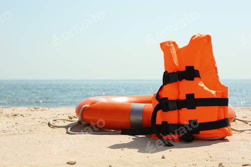 Preview: Orange life jacket and buoy on sandy beach near sea. Emergency rescue equipment