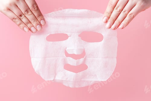Preview: Female hands hold white fabric mask on pink background.