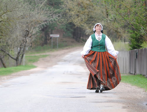 Preview: an elderly woman in the Latvian national folk costume on an empty country road