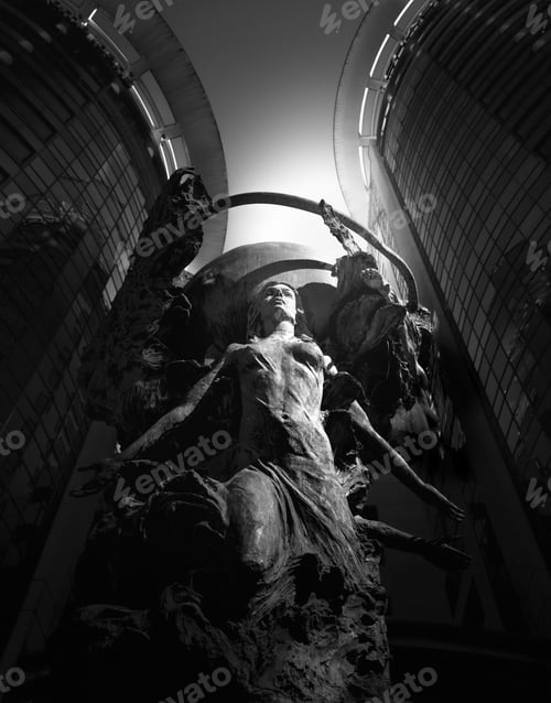 Preview: an abstract sculpture with multiple heads sitting on a statue and two people walking past