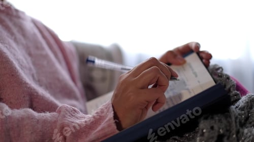 Preview: unrecognizable woman in warm knitted sweater writes down plans or tasks for the new year.